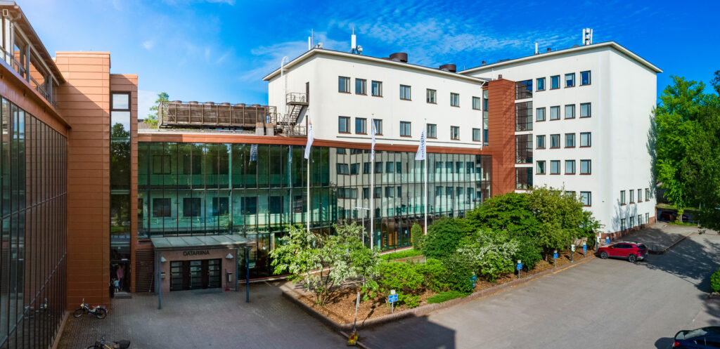 Yritystalo Datariina edestäpäin kuvattuna. Edustalla parkkipaikka ja vehreitä kasveja.