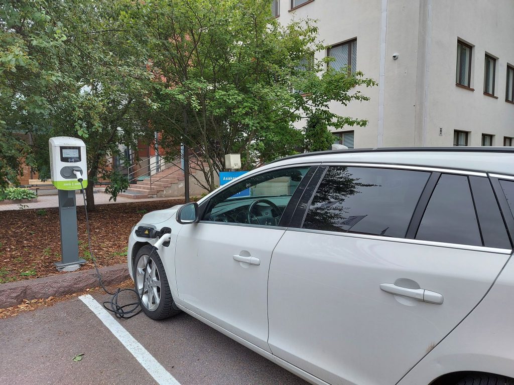Valkoinen sähköauto latauksessa.